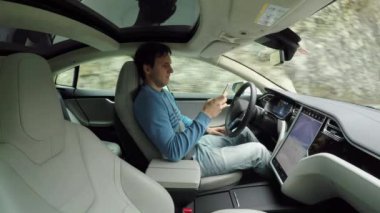 Otomatik otomatik pilotlu elektrikli araba kullanırken sürücü cep telefonunu tutuyor.