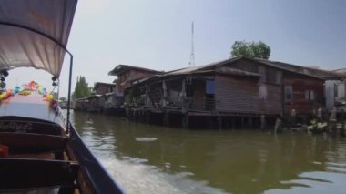 LOW ANGLE: Wooden longtail boat speeding past poor neighborhood on smelly river