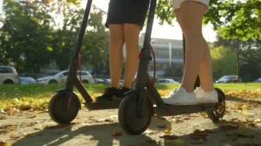 Yavaş hareket, düşük öfke, yaklaşma, güneş ışığı: Etekli tanınmayan kadınlar, güneşli cadde boyunca elektrikli scooterlara biniyorlar. İki bayan arkadaş yüksek teknolojili e-scooterlarla parkta dolaşıyorlar.. 