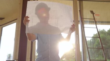 SLOW MOTION, CLOSE UP, LENS FLARE: Male architect looks at his floor plans for the modern timber house on a sunny day. Construction site supervisor checks the progress of important real estate project