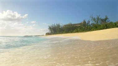 Barbados 'taki kumlu sahili silip süpüren kristal berrak deniz dalgalarının düşük açılı görüntüsü. Camsı dalgalar, güneşli Karayipler 'de okyanus kıyısındaki bir otelin yanındaki beyaz kumlu sahili yıkıyor..