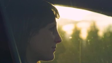 Yaklaş, LENS FlaRE, DOF: genç bayan sürücü kırmızı ışıkta beklerken düşüncelere dalıyor. Beyaz kadın gün batımında arabasında otururken gülümsüyor. Altın güneş ışınları bin yıl boyunca arabada parlar..