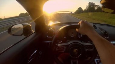 SLOVENIA, AĞUSTOS 2020: POV: Yeni bir Porsche spor arabasını Slovenya kırsalında uzanan boş bir asfalt otobanından sürerken kokpitin içinde altın akşam güneşleri parlıyor