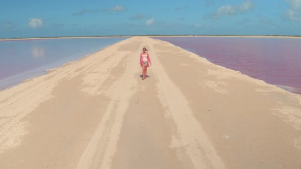 女游客在穿越五彩缤纷的盐田的土路时旋转着 无忧无虑的女人伸出手去探索墨西哥那些粉红发亮的盐场 — 图库视频影像