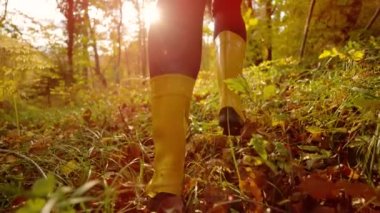 Yavaş hareket, lensler, düşük açı, yakın çekim: Sonbahar renkli ormanda koşan çizmeli bir kızın sinematik görüntüsü. Sarı lastik çizme giyen kadın sonbaharda cennet ormanında koşar renk değiştirir..