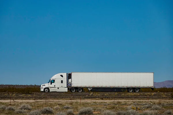 CLOSE UP: White semi-trailer truck hauls a heavy cargo container across a desert in the United States. Unmarked freight lorry speeds along the scenic interstate highway crossing the vast Utah desert.