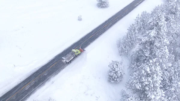 雪の積み重ねトラックは ホワイトアウト中に常緑の森をリードする国の道路をきれいにします 雪の上を飛んで新鮮な雪のアスファルトの道路をクリアする 危険な道路状況 — ストック写真