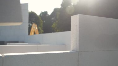 Human hand laying bricks for building a wall on a garden terrace on a sunny day. Use and work with hardscape materials at unfinished summer construction project. Grey wall construct in the backyard.