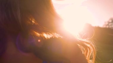 Look over the shoulder of beautiful woman watching sunset. Summer evening breeze gently moving the long wavy hair of a beautiful woman illuminated with amazing golden light