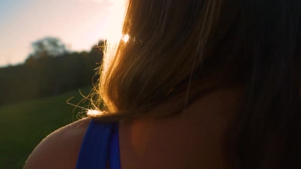 夕日を見てかなり若い女性の肩のビューで 夏の夜の風優しく素晴らしい黄金の光で照らされた美しい女性の長い波状の髪を移動 — ストック動画