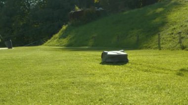 CLOSE UP: Automated robotic lawn mower trimming green grass in summer garden. Futuristic gardening equipment for lawn mowing doing a precise job in modern garden. Garden robot at work in backyard.