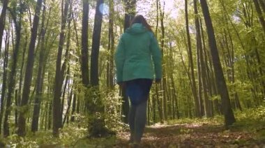Bahar yeşili kayın ormanı ve yolda yürüyen sportif bir kadın. Yaprak döken ormanlık alanda şaşırtıcı bir bahar uykusundan uyanmış doğa. Etrafını çevreleyen yeşilliklerin arasında dinleniyor..