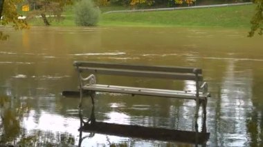 Sonbahar yağmurundan sonra akan bir nehrin kirli taşkın suyunda beyaz park bankında. Nehir kıyılarını, taşan çimenleri ve ağaçları delen çamurlu sular. Şiddetli sağanak ardından şiddetli seller.