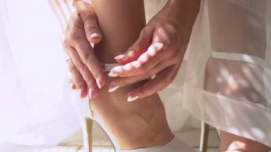 Gelinin elleri, güzel beyaz düğün ayakkabılarının bilekliklerini taksın. Kendisini düğün gününe hazırlarken otantik prosedürler uygulanacak. Şık bir gelinlik için şık ayakkabılar..