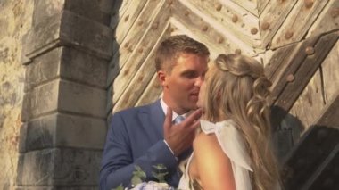 Romantik yeni evliler, tahta kapıların önünde sevgi dolu bir öpücük paylaşıyorlar. Güzel genç çift aşklarını evlilikle mühürledi. Neşeli gelin ve damat arasında romantik bakışlar ve şefkat.