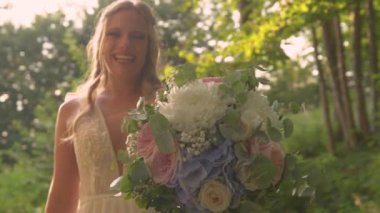 Mutlu gelin tarafından tutulan yumuşak pastel renkte güzel bir buket çiçek. Gururla düğün gününde altın gün batımında muhteşem bir buket yaz çiçeği gösteriyor..