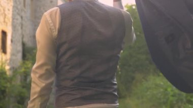 Damadın düğün ceketini omzunun üstünden fırlatırkenki dikiz görüntüsü. Genç ve zarif damat, düğün gününde muhteşem altın gün batımı ışığında eski kale duvarlarının orada yürüyor..