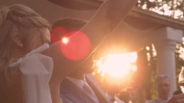 LJUBLJANA, SLOVENIA, HAZİRAN 2023 LENS FLARE, KAPALI: yükseltilmiş şampanya kadehleriyle mutlu yeni evliler. Düğün resepsiyonunda kadeh kaldırırken şampanya kadehlerinde altın güneş ışınları parlıyor..