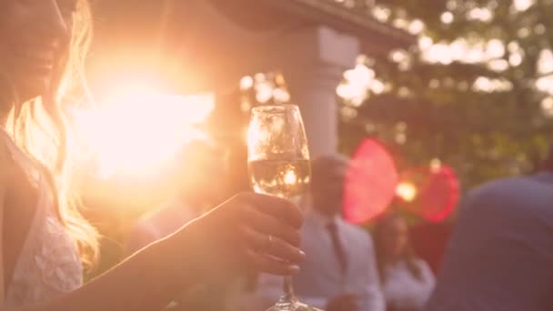 Ljubljana Slovenia エイプリル2023 レンズフレア クローズアップ 輝くシャンパングラスを持ち上げる笑顔の花嫁 結婚式のレセプションで乾杯しながら シャンパングラスを通して黄金の太陽の光が輝きます — ストック動画