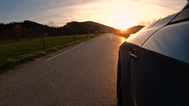 金秋日落时 辛尼蓝色的车沿着弯曲的乡间道路行驶 在美丽的日出时分 一辆跑车在乡间小路的弯道上疾驰而过 其特写镜头的角度很低 — 图库视频影像