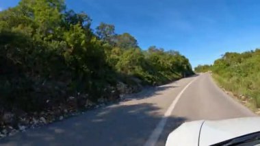 Mavi gökyüzünün altında asfalt yol boyunca uzanan beyaz bir araba. Kayalık araziye oyulmuş ve Adriyatik 'in güneşli adası Hvar' da yeşil çam ağaçlarıyla çevrili asfalt yollar..