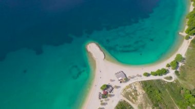 Güzel kumlu sahildeki küçük yarımadayı çevreleyen çarpıcı mavi deniz. Biokovo dağlarının altındaki Makarska 'nın turistik bölgesinde beyaz kum ve kristal berraklığında muhteşem deniz kıyısı.