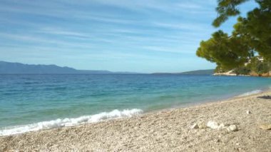 Hafif kristal mavisi Adriyatik Denizi dalgaları ve güneşli bir yaz gününde çakıl taşı plajı. Dalmaçya 'nın güzel kıyılarındaki dalgalı deniz suyunun rahatlatıcı manzarası. 