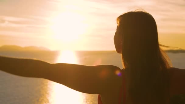 レンズフレア 閉じる 美しい女性が日の出を見ながら腕を伸ばしています 彼女は素晴らしい景色を賞賛しており 絵のように美しいダルマチアの海に静かに広がる夏の太陽の最初の光線を見ています — ストック動画