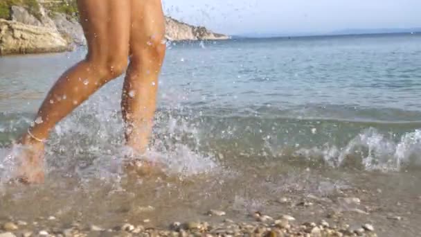 スローモーション クローズアップ 浅い海を走っている間に遊び心のある女性が水を噴出します 彼女はHvarの日当たりの良い島の素晴らしい海岸線に囲まれた屈託のない夏休みを楽しんで楽しんでいます — ストック動画
