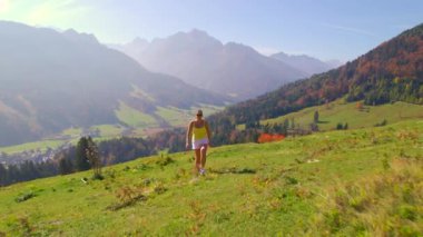 Sonbahar yürüyüşü sırasında köpeğiyle birlikte manzaralı bir dağ çayırında gülümseyen kadın. Güneşli bir günde, sonbahar mevsiminin renkli gölgelerinde dağların ve yemyeşil ormanların manzarasının tadını çıkarıyor..