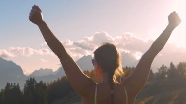 Yaklaşın, LENS FlaRE: manzaralı dağ zirvesine ulaşan bir bayanın zafer anı. Kollarını kaldırıp, sonbahar günbatımında dağların muhteşem manzarasını kutluyor..