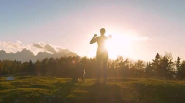 Yaklaş, LENS FlaRE: kadın altın ışıkta tepede kollarını kaldırır. O, köpeğiyle yokuş yukarı koştuktan sonra pitoresk bir zirveye ulaşmayı kutluyor. Dağlarda güzel bir sonbahar günü