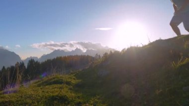 Yaklaş, LENS FlaRE: hayati adam koşar ve çimenli yolda köpeğiyle atlıyor. Çevik arkadaşlar, güzel sonbahar günbatımında, pitoresk dağlık çayırlarda iz bırakmadan otlak patikada hızla koşarlar..