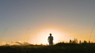 Gülümseyen adam gün batımında köpeğiyle tepeye koşarken neşeyle zıplar. Mutludur ve altın sonbahar günbatımında resimli dağların zirvesine ulaştığında zaferi hisseder..