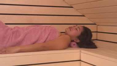 Genç Filipinli kadın, Finlandiya saunasında uzanıyor ve dinleniyor. Güzellik merkezinde vücudunu arındırmak ve tazelemek için kendine sakinleştirici ve sıcak bir sauna terapisi uyguluyor..