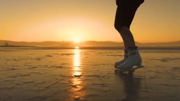 レディースフリーア シルボウテ 黄金の日没ライトでスケートする白いアイススケートの女性 アクティブな若い女性は氷のスケートですが 冬の太陽の最後の光線は自然に凍った湖の表面を反映しています — ストック動画