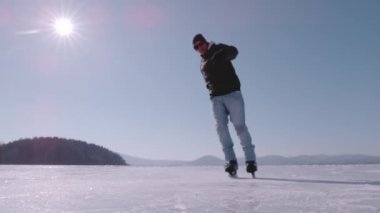 Genç adam patenlerin üzerinde fren yaptığında, buz parçalarını uçuran süper yavaş hareket. Aktif adam büyük donmuş bir gölde buz pateni yapıyor ve hokey antrenmanı yapıyor. Kış aktiviteleri için güzel güneşli bir gün.