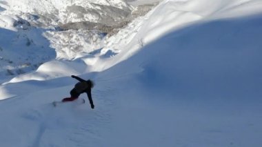 Genç bayan snowboard yaparken taze ve derin kar içinde yuvarlanıyor. Güneşli bir kış günü, karlı bir dağlık bölgede snowboard yaparken gülümsüyor ve eğleniyor..
