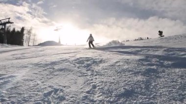 Gülümseyen kadın kayak yapıyor ve kameraya doğru kar püskürtüyor. Neşeli bayan kış tatilinde ve güzel güneşli bir günde Avusturya Alplerindeki karlı kayak merkezinde kayak yapmaktan hoşlanıyor..