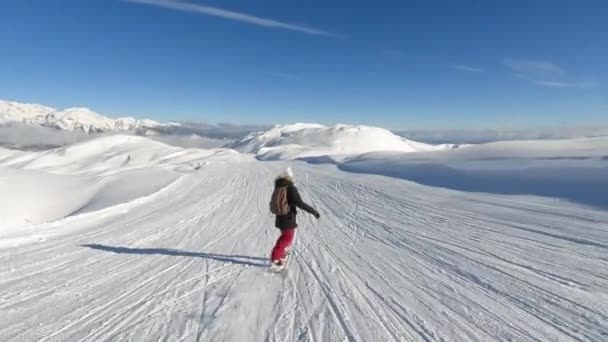 雪山の素晴らしい景色を望む美しいスキー場でスノーボードをしています 彼女はアルペンスキーリゾートで美しい晴れた冬の日に新鮮な雪と成長したスキー場でスノーボードに乗っています — ストック動画