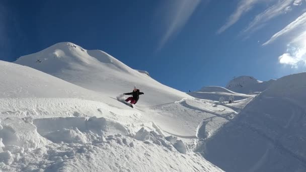 スノーボード アクティブな女性はスノーボードしながら粉雪の大きな雲をスプレーします 彼女は晴れた冬の日にスロベニアアルプスの中心部に新しく雪が降らない山のテラスでスノーボードに乗っています — ストック動画