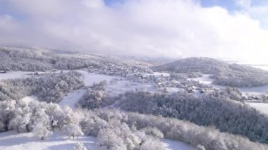 Tepedeki şirin, küçük bir köy, üzerinde taze bir kış battaniyesi var. Kar yağdıktan sonra güneşli bir günde karlı bir tepenin harika manzarası. Kırsal alanda beyaz kış harikalar diyarı.