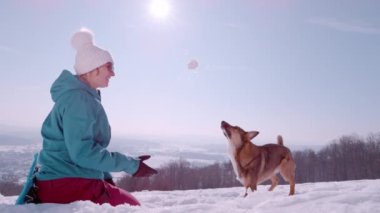 Gülümseyen kadın, sevimli, oyuncu köpeğine bir kartopu atar ve o da onu havada yakalar. Leydi ve köpeği güneşli bir kış gününde yürüyüş yaparken karla oynamaktan zevk alırlar..