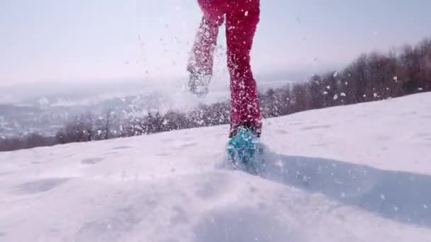 レンズフレア Slow Motion Close 遊び心のある若い女性は 晴れた日に新しく落ちた雪の中でスノーシューで走っています スノーシューで下り坂を走り 雪をスプレーする女性の後 — ストック動画
