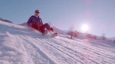Güneşli bir kış günü, karlı tepeden kayan bir bayanla birlikte. O gülümsüyor ve plastik kar kızağında sürmekten hoşlanıyor. Karlı dağlarda eğlenceli ve adrenalin dolu açık hava aktiviteleri.