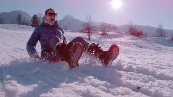 スローモーション クラスアップ ハッピーな若い女性は雪の丘を下りることを楽しんでいます プラスチック製のスノーソリッジで滑っている間 彼女は微笑み 興奮しています アルプス渓谷での楽しい屋外冬のアクティビティ — ストック動画