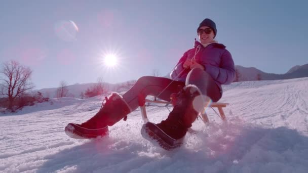スローモーション クラスアップ 美しい女性は木製のソリでスライドを楽しんでいます 冬の太陽が輝き 雪の丘を下りながら微笑んでいる アルプスの楽しい屋外アクティビティ — ストック動画