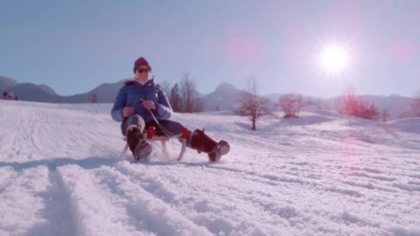 スローモーション Close 陽気な若い女性は美しい冬の日に雪の斜面を滑ることを楽しんでいます 太陽は輝いていて 木製のスリーガーに乗って通り過ぎると雪が輝いています — ストック動画