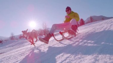 Güneşli bir kış gününde, karlı tepeden kayarak inen bir adam var. Gülümsüyor ve yanında köpeği ile ahşap kar kızağında sürmekten hoşlanıyor. Alp Vadisi 'nde eğlenceli aktiviteler.