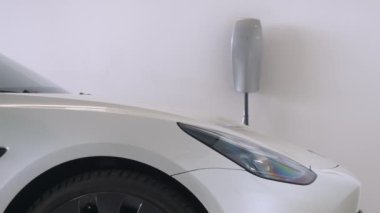 GARAGE 'DA TESLA CARAHI, Kasım 2023: Ev garajında motorlu akü şarj eden beyaz bir Tesla arabasının ön kısmı. Konut binalarında elektrikli araca güç sağlamak için etkin bir sistem.